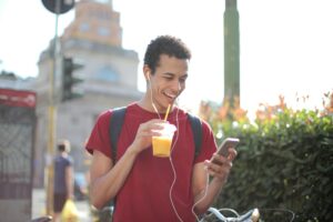 cheerful man with smartphone drinking juice on street